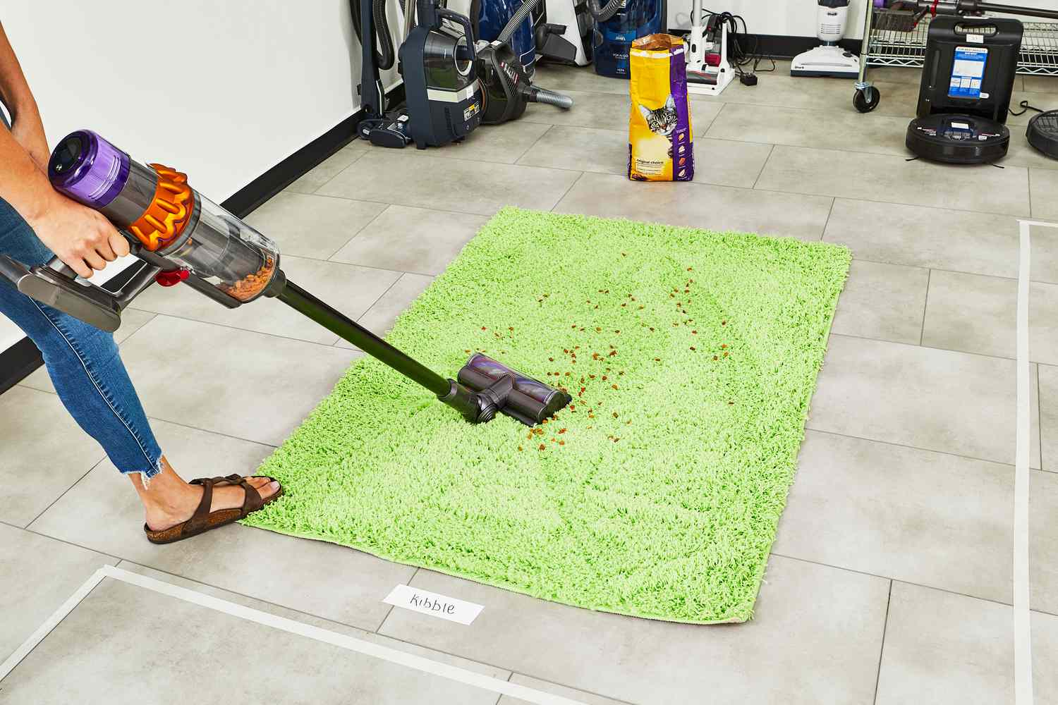 A person using a Dyson V15 Detect Cordless Vacuum Cleaner to clean pet food from a green carpet