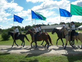 five horses, with riders carrying colorful flags